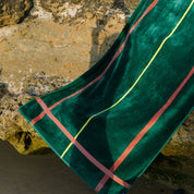 Green beach towel with cognac and yellow lines draped over a stone surface