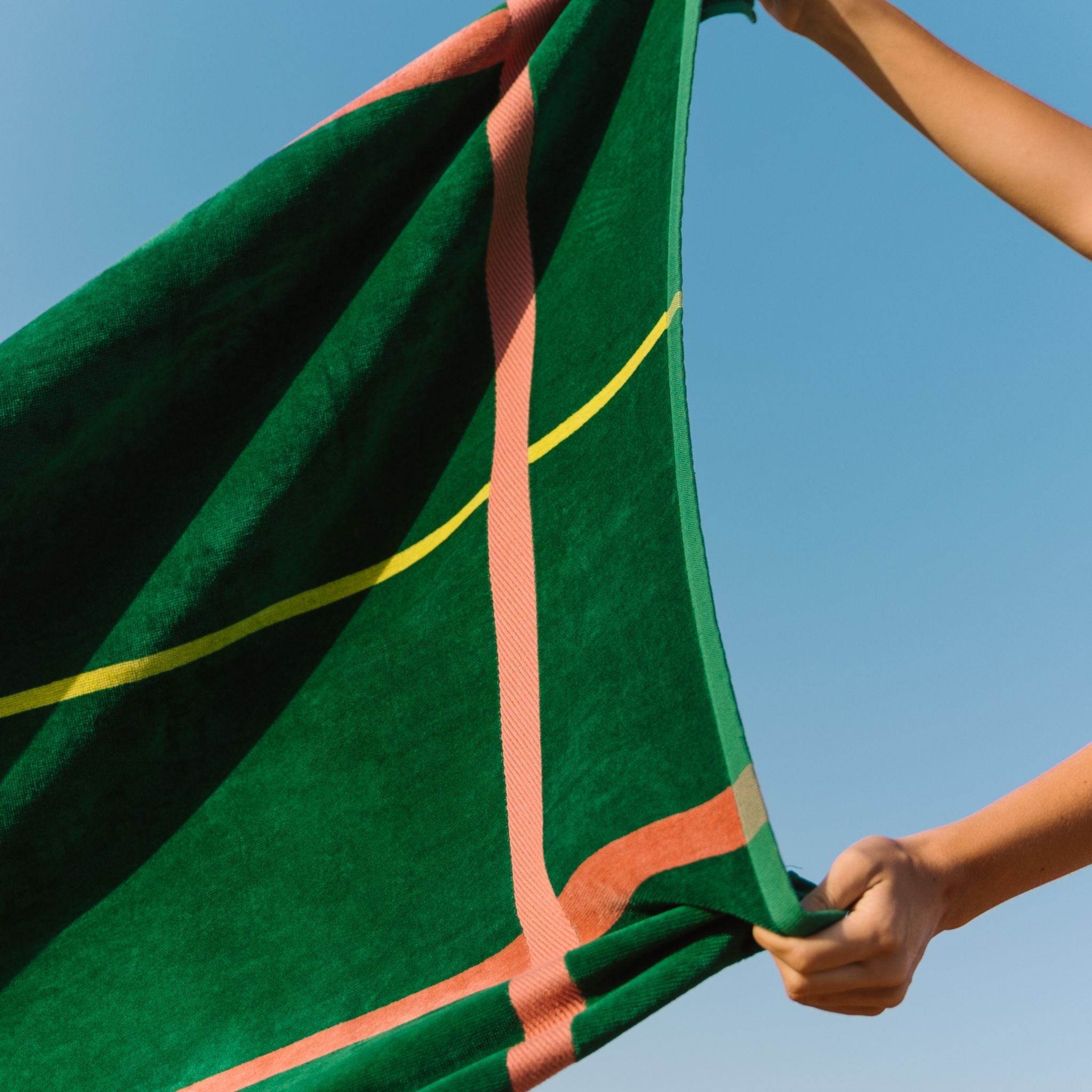 Green and cognac striped beach towel held against a clear blue sky