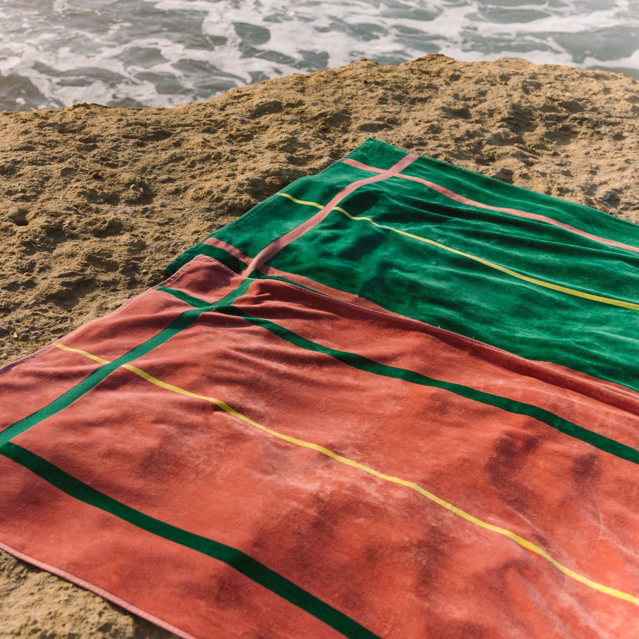 Cognac and green striped beach towel on a sandy beach with ocean waves in the background