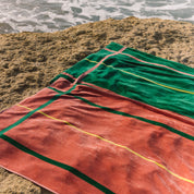 Cognac and green striped beach towel on a sandy beach with ocean waves in the background