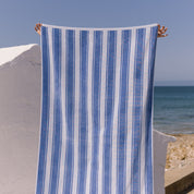 Blue striped beach towel held up against a beach backdrop