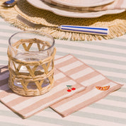 Woven glass on a striped tablecloth with a striped napkin featuring embroidered designs of orange and cherry.